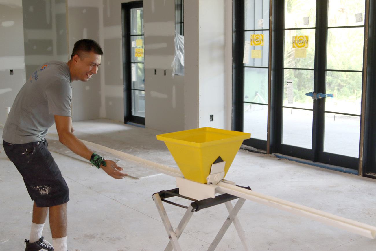 The picture depicts a construction worker on a job site. There is a yellow construction tub sitting on a stool.