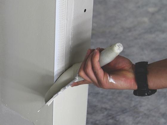 A Trim-Tex worker is applying joint compound on a drywall corner bead.