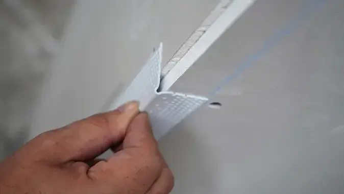 This image depicts a corner bead being held up to drywall.